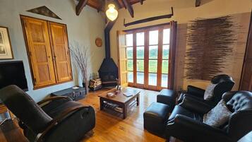 Una sala de estar acogedora con chimenea, muebles de madera y grandes ventanales que ofrecen vistas al exterior.