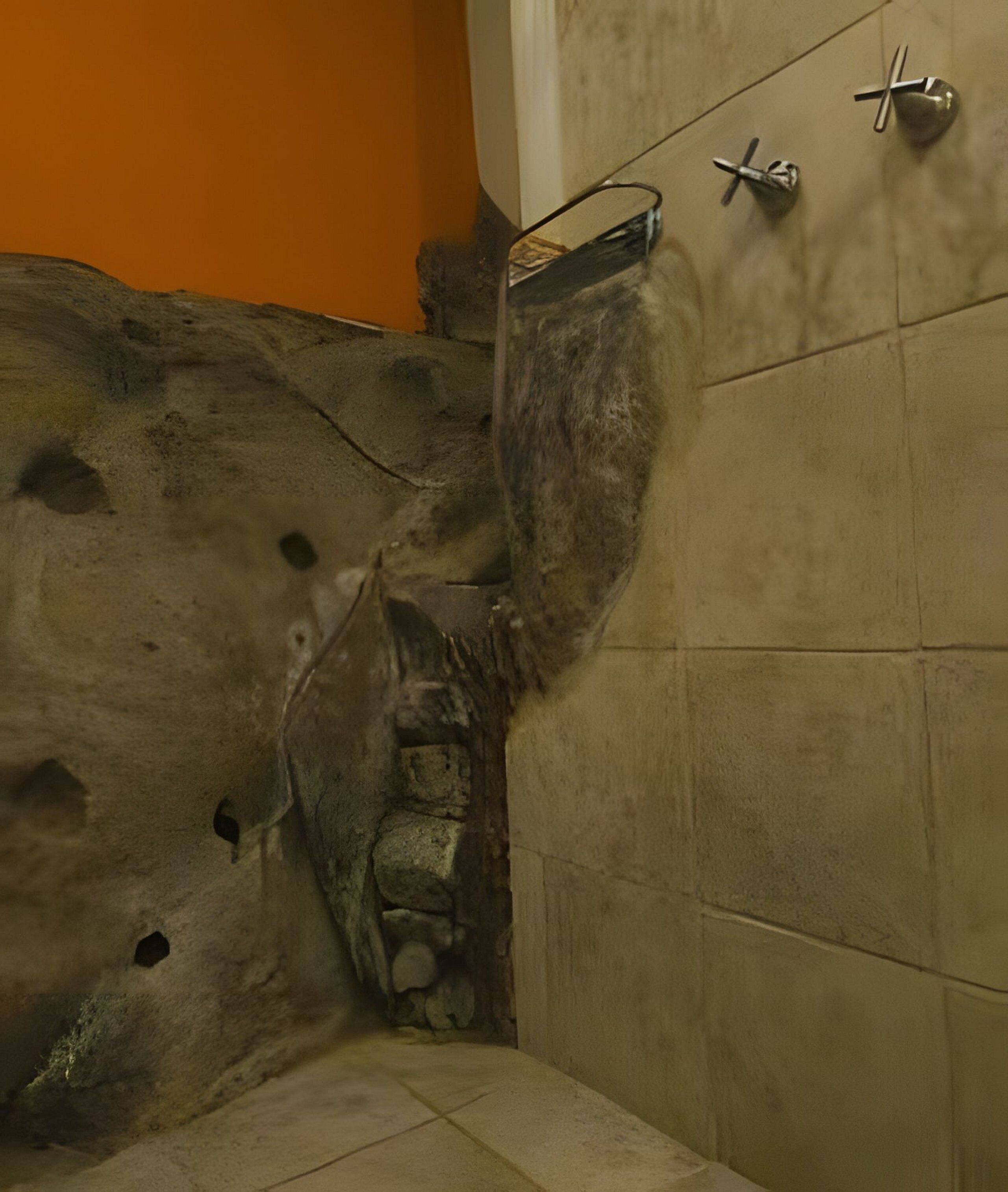 Bagno con parete in pietra, zona doccia e pavimento piastrellato.
