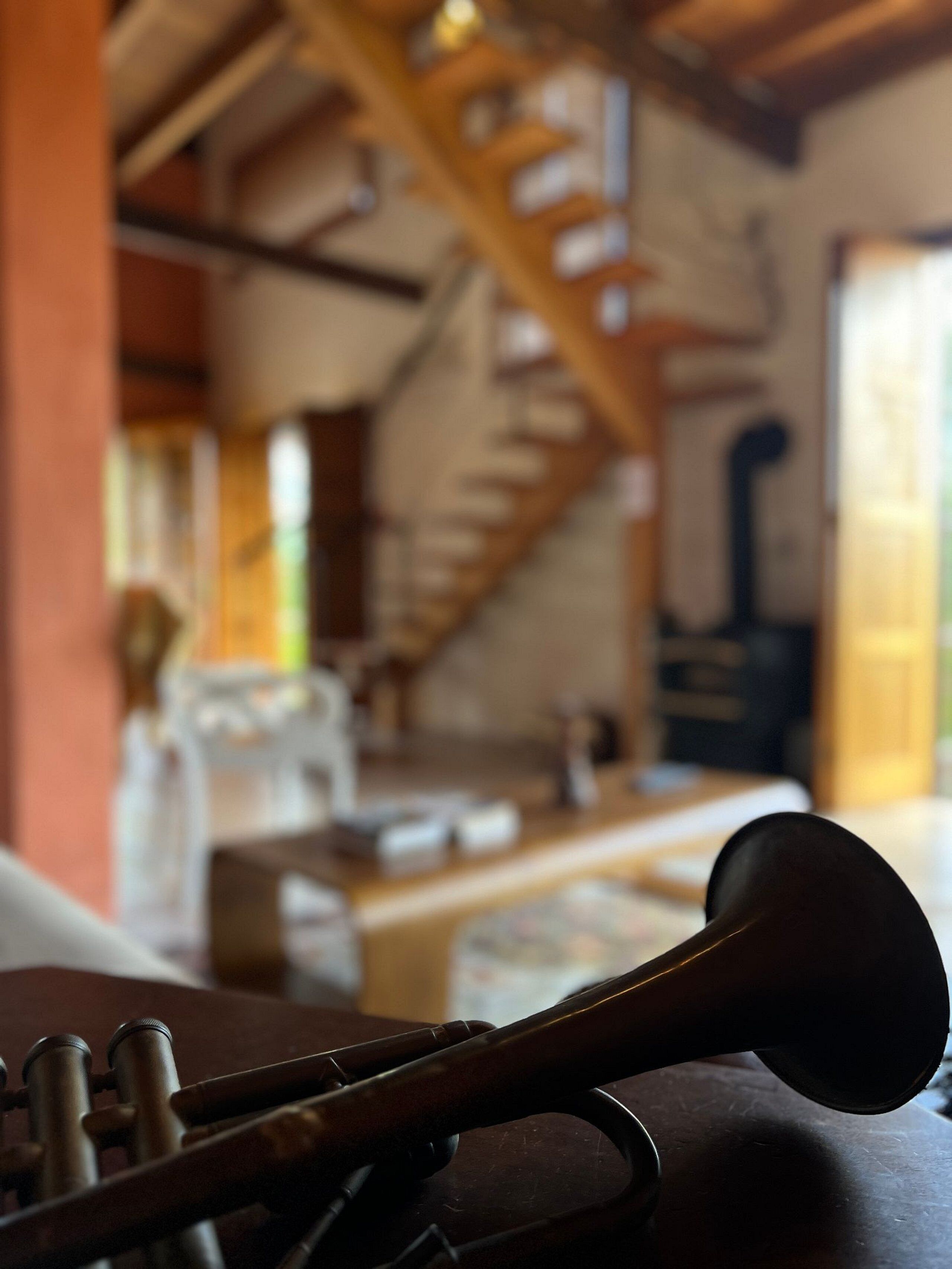 A close-up of a wooden musical instrument, possibly a banjo, with a blurred background featuring a staircase and a fireplace.