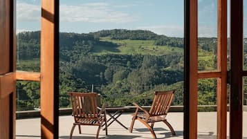Une porte en bois ouverte, avec deux chaises en bois et une petite table sur un balcon donnant sur un paysage verdoyant.