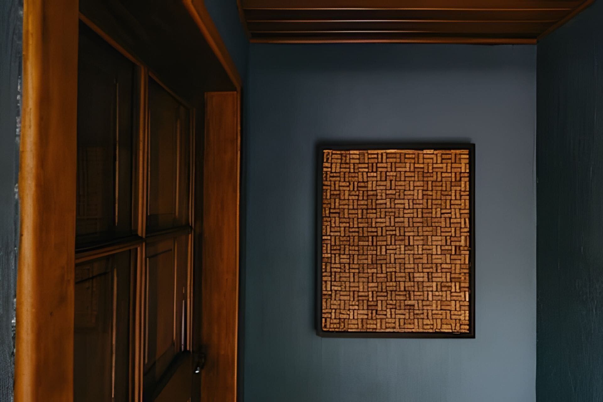 A room with a dark blue wall, a wooden door, and a framed wall hanging with a geometric pattern.