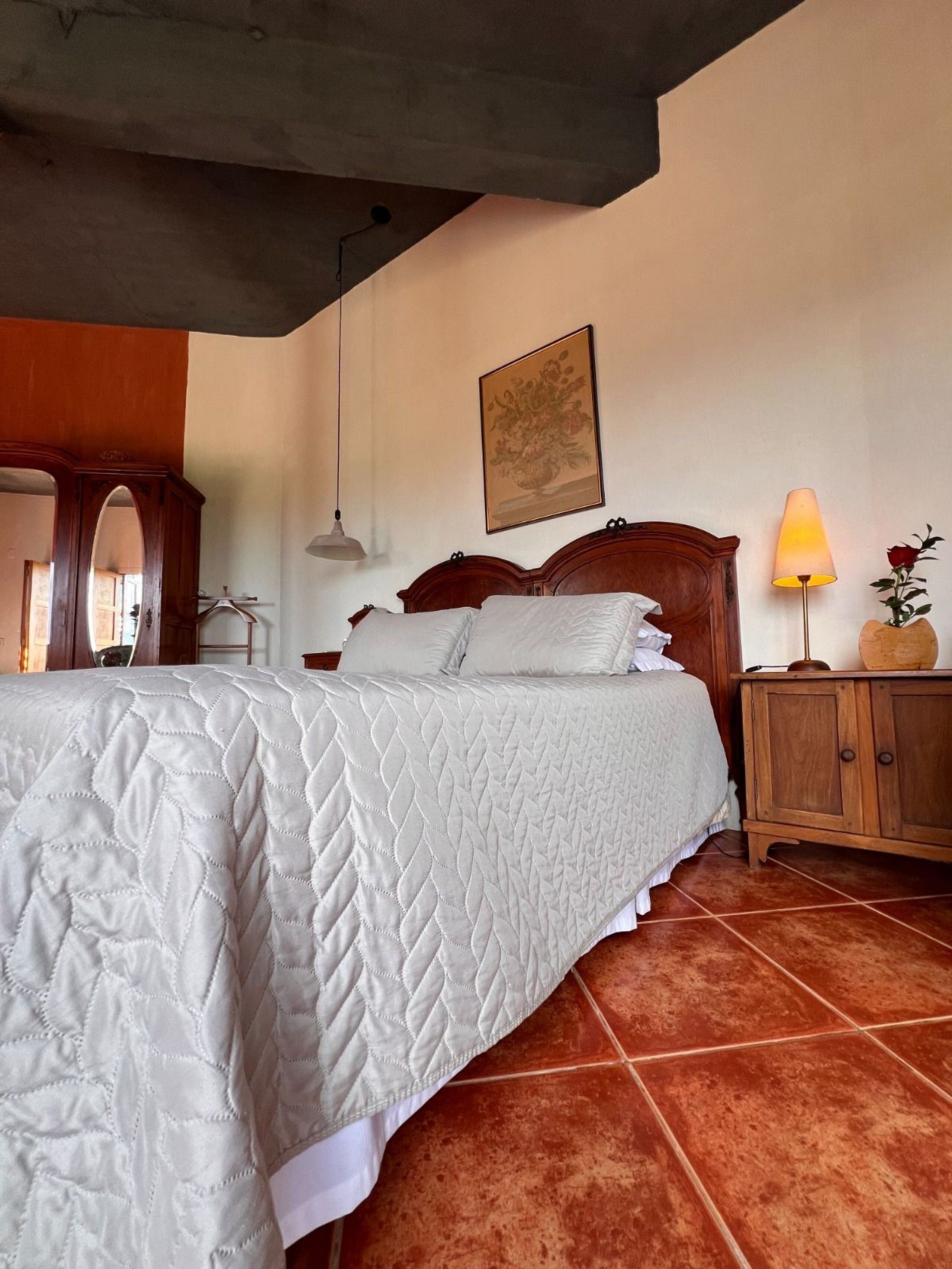 A bedroom with a large bed, a wooden headboard, a nightstand, a lamp, and a framed picture on the wall.