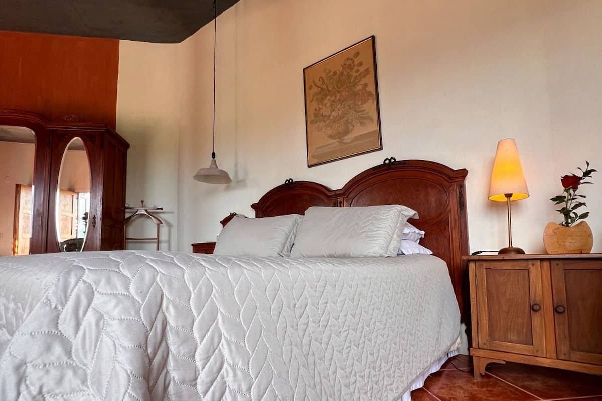 A bedroom with a large bed, a wooden headboard, a nightstand, a lamp, and a framed picture on the wall.