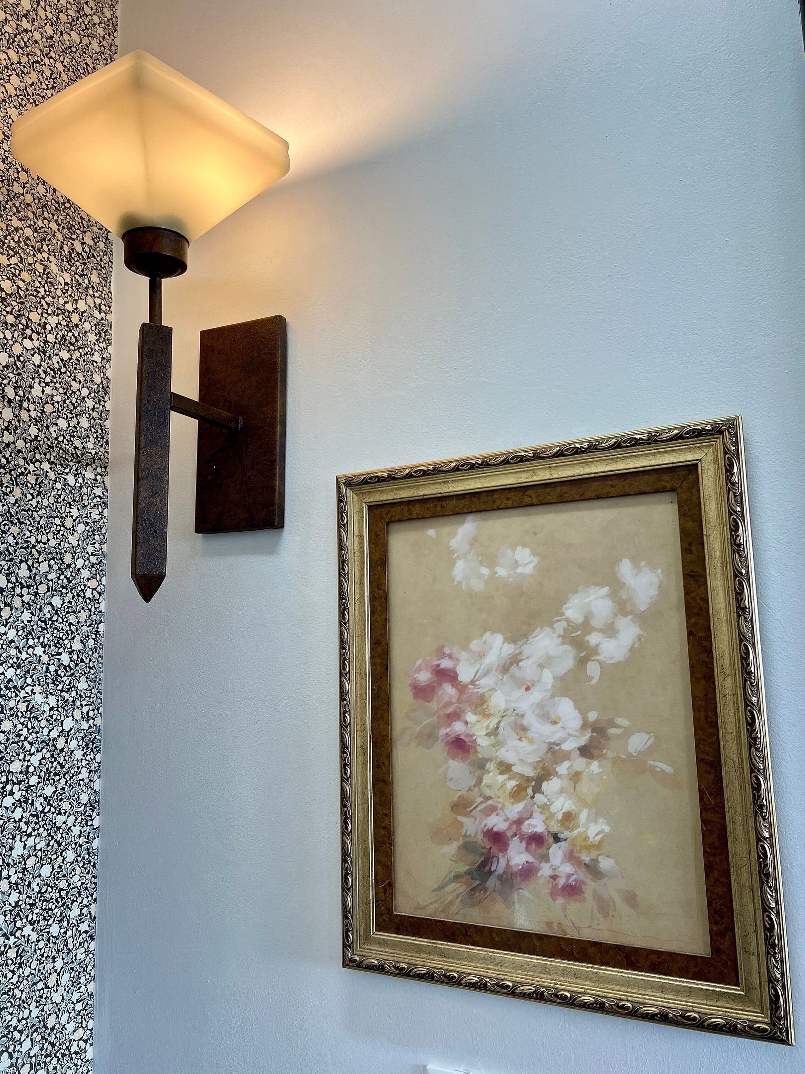 Una lámpara de pared y un cuadro enmarcado con flores.
