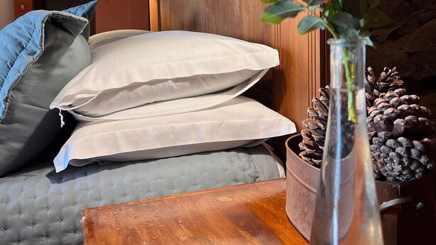 A bedroom with a bed, pillows, a vase with a flower, and a wooden nightstand. - Pousada Borghetto (Bento Gonçalves)
