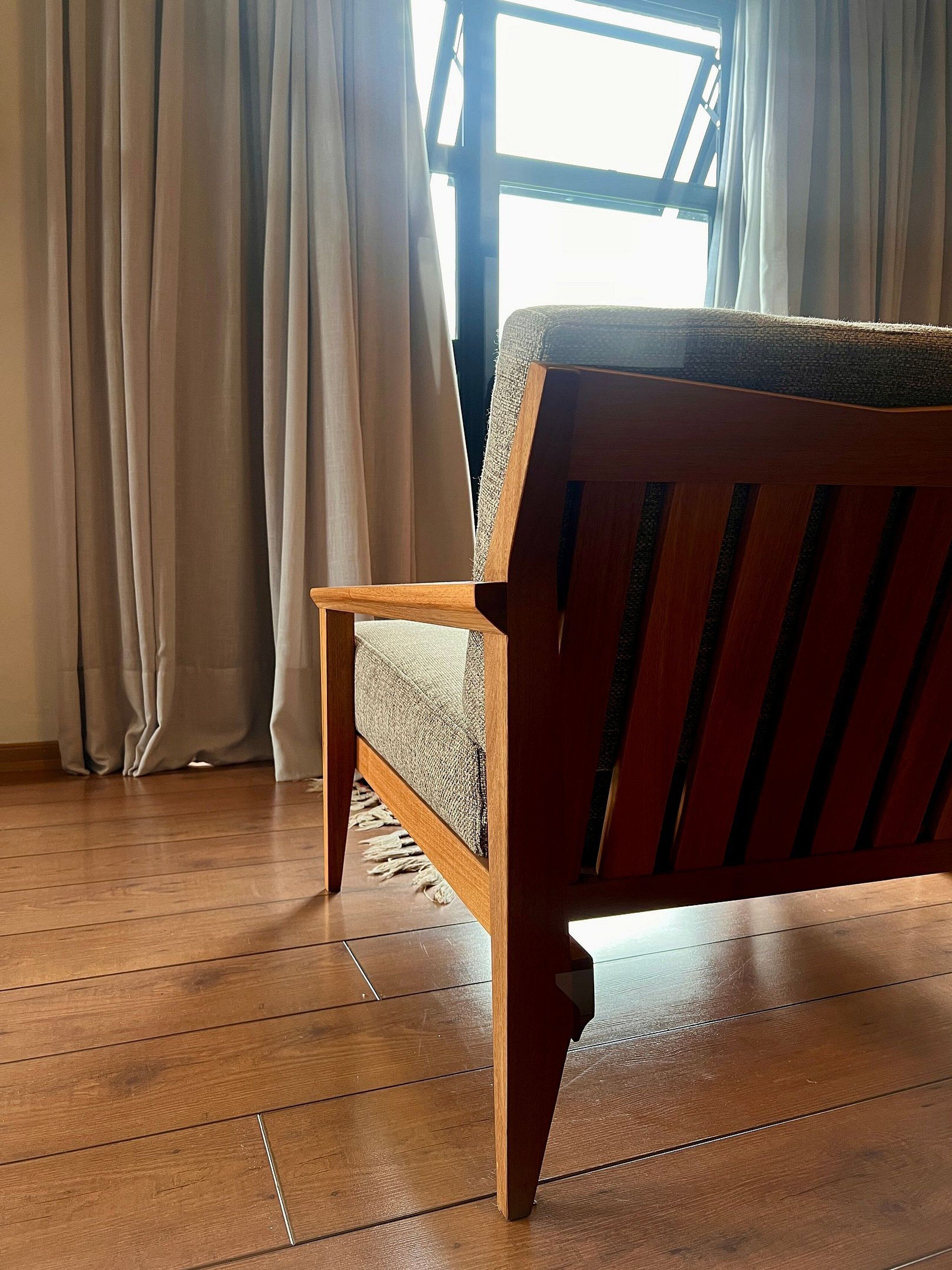 Una silla de madera con asiento y respaldo trenzados, ubicada en una habitación con piso de madera y una ventana con cortinas.