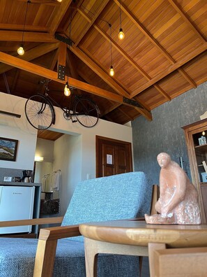 A room with a wooden ceiling, a bicycle hanging from the ceiling, a chair, a table, and a statue. - Pousada Borghetto (Bento Gonçalves)