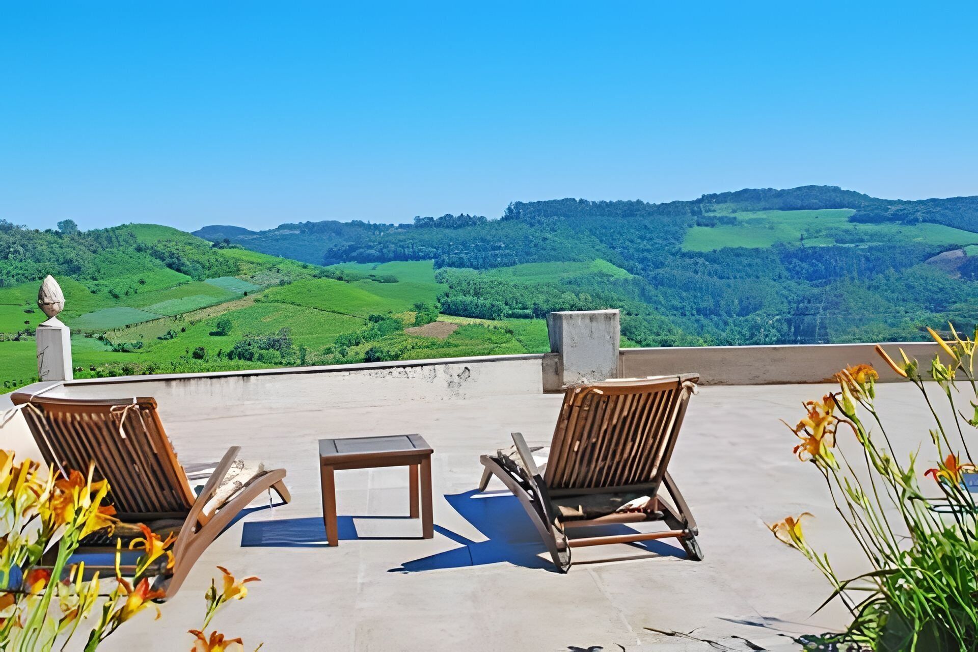Une terrasse avec deux chaises en bois et une petite table, donnant sur un paysage verdoyant et luxuriant.