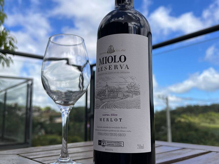 A bottle of Molo Reserva Merlot wine and a wine glass on a wooden table with a scenic view in the background.