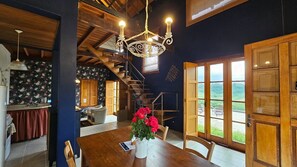 A dining area with a wooden table, chairs, and a chandelier. There is a staircase leading to another level, and a view of the outdoors through large windows. - Pousada Borghetto (Bento Gonçalves)