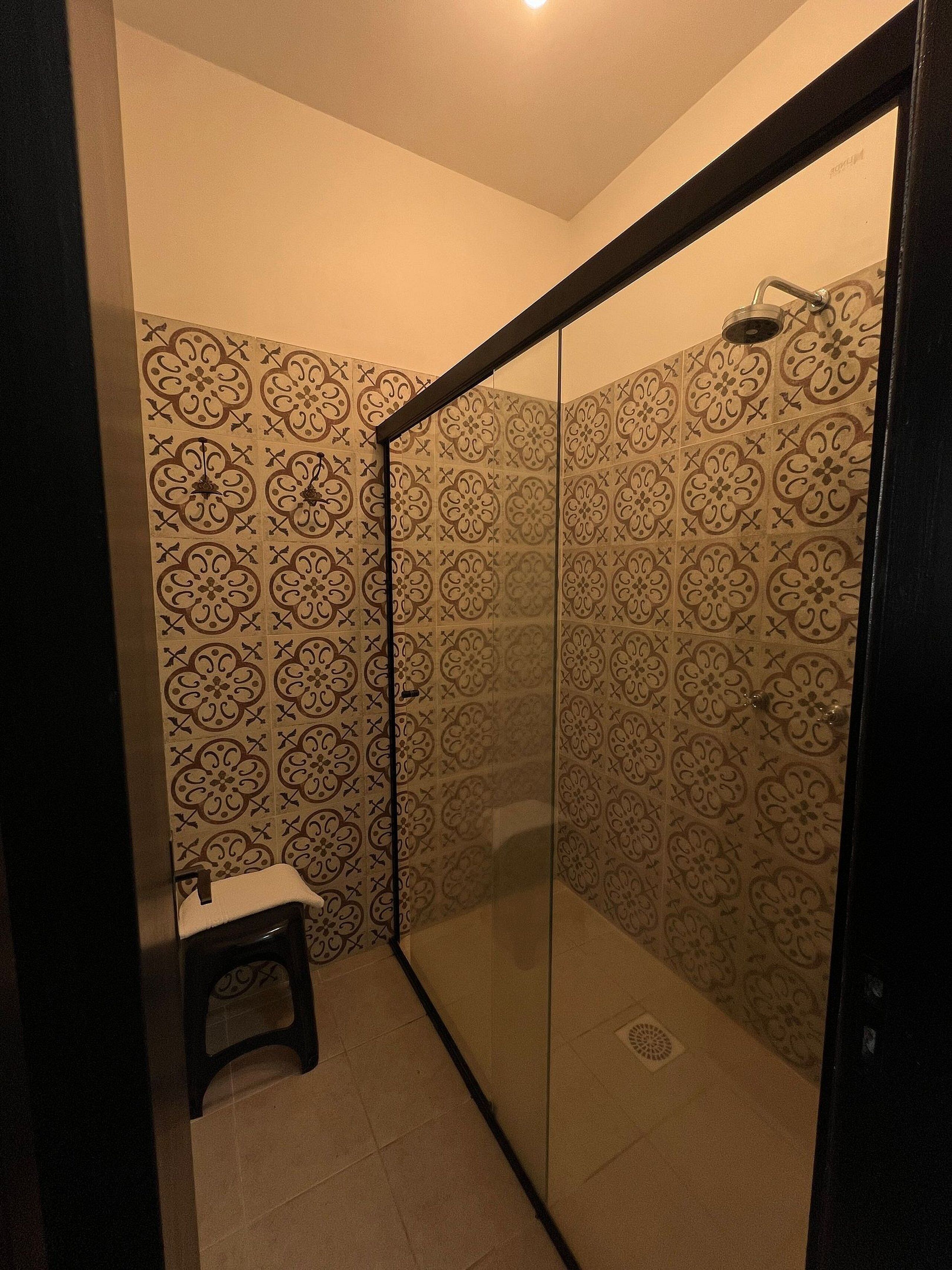 Um chuveiro pequeno e fechado, com azulejos estampados e divisória de vidro.