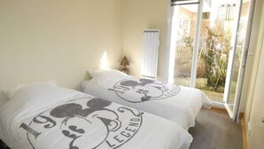 Een slaapkamer met twee bedden, elk voorzien van een kussen met het Mickey Mouse thema, een raam met uitzicht op de omgeving en een schuifdeur naar een balkon.