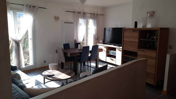 Een woonkamer met een bank, salontafel, televisie en een eethoek met stoelen en een tafel.