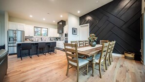 A modern kitchen with white cabinets, a central island, and a dining area with wooden chairs and a table. - Welcome to PEDAL AND PLUNGE (Bella Vista)
