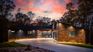 A modern two-story house with a stone exterior and a dark facade, featuring a driveway and a small patio area. - Welcome to PEDAL AND PLUNGE (Bella Vista)