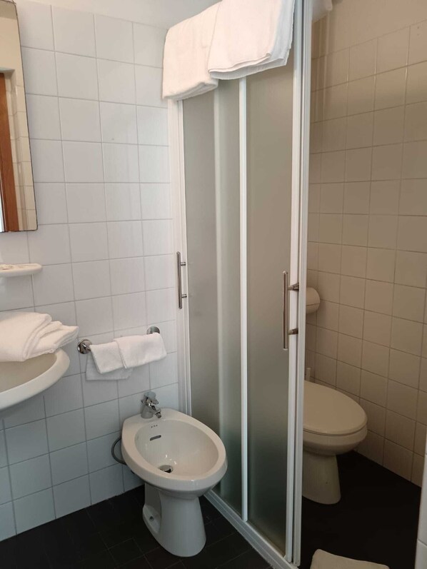 Une salle de bain équipée d’un bidet, de toilettes et d’une douche à parois de verre.