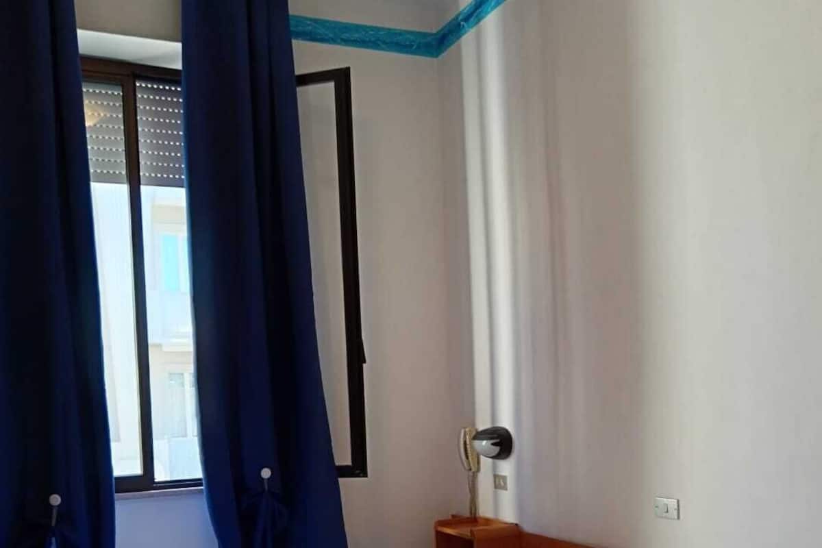 A bedroom with a bed, a nightstand, a lamp, and a window with curtains.