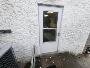 A white door with a window, a metal air conditioning unit, and a textured wall.