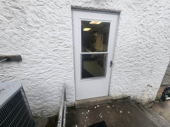 Una puerta blanca con ventana, un equipo de aire acondicionado metálico y una pared con textura.