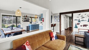 Un salon moderne avec un canapé marron, un coin repas doté d’une grande table et une cuisine en arrière-plan.