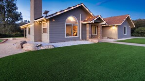 Une maison moderne avec un grand jardin à l’avant, une cheminée et une pelouse bien entretenue.