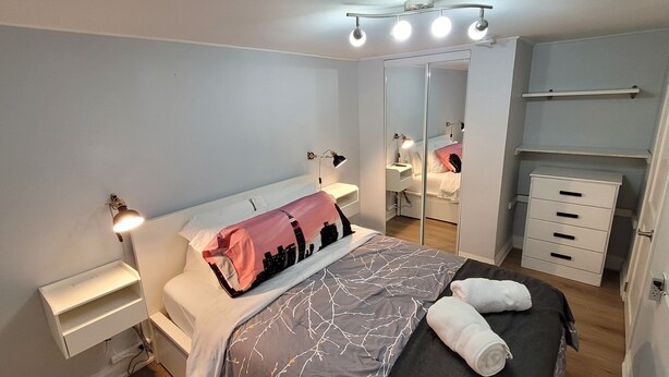 A modern bedroom with a bed, bedside lamps, a wardrobe, and a mirror. - A Basement Studio for 2 (Brampton)