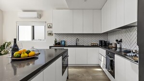Une cuisine moderne avec des meubles blancs, un dosseret en carreaux disposés en chevron et un îlot central agrémenté de fruits.