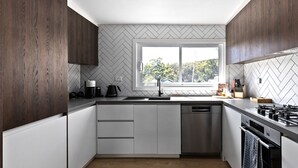 A modern kitchen with a herringbone-patterned backsplash, a window with a view of greenery, and stainless steel appliances. - Fox on Church - pet friendly 2 bedroom home (Hepburn Springs)