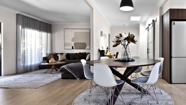 A modern living room with a dark grey sofa, a round dining table with white chairs, a grey rug, and a wooden floor. - Fox on Church - pet friendly 2 bedroom home (Hepburn Springs)