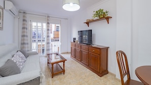 Una sala de estar con un sofá, una mesa de centro, un televisor sobre un mueble de madera y una mesa de comedor con una silla.