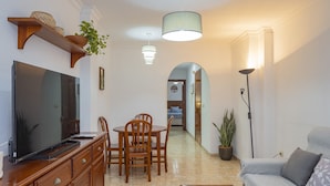 Una sala de estar con televisor, muebles de madera, un sofá y un comedor con sillas y una mesa.