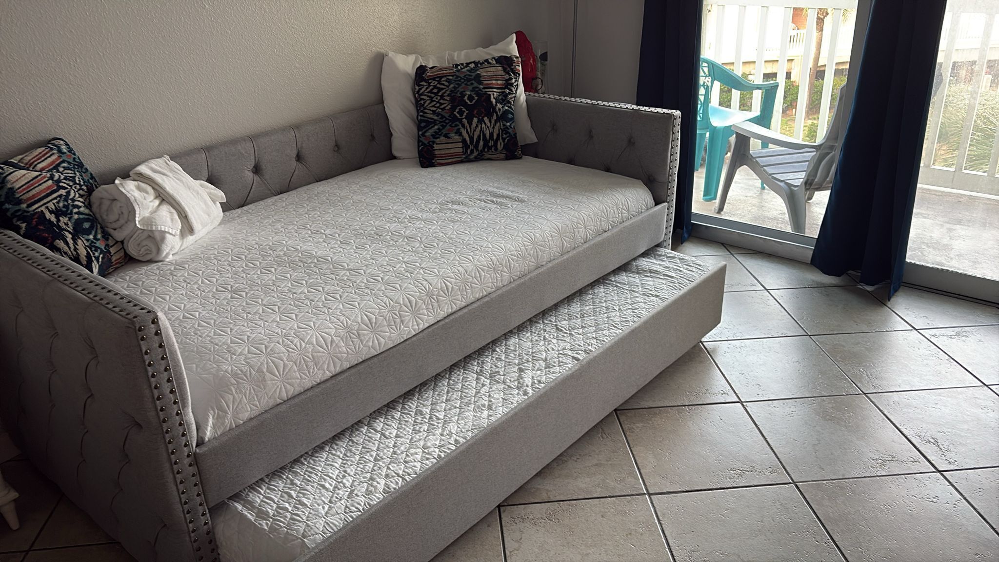 Ein graues Sofa mit gemustertem Bezug, eine kleine erhöhte Plattform und Blick auf einen Balkon mit Stühlen.