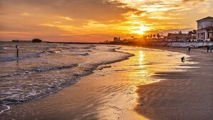 A beach with a sunset, waves, and a pier in the background. - Ocean & Pool View Top Floor | 2 Pools| HotTub |GYM (Galveston)