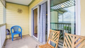 A covered porch with yellow siding, a blue plastic chair, and a wooden chair. - Ocean & Pool View Top Floor | 2 Pools| HotTub |GYM (Galveston)