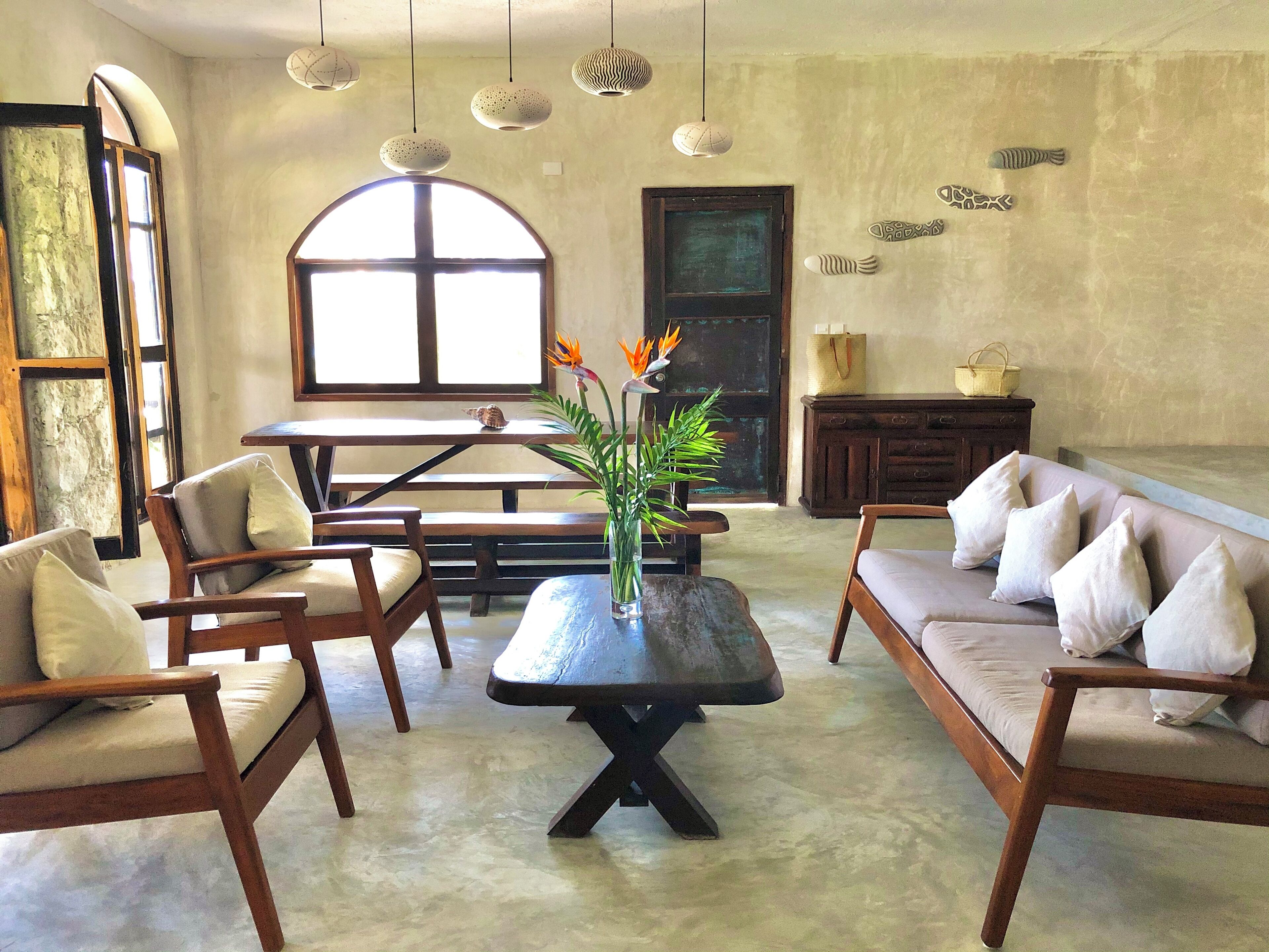 A spacious room with a wooden sofa, two armchairs, a dining table, and a large window.