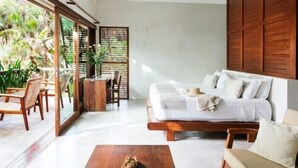 A modern room with a bed, a wooden coffee table, and a dining area with chairs and a table. - Olas Tulum (Tulum)