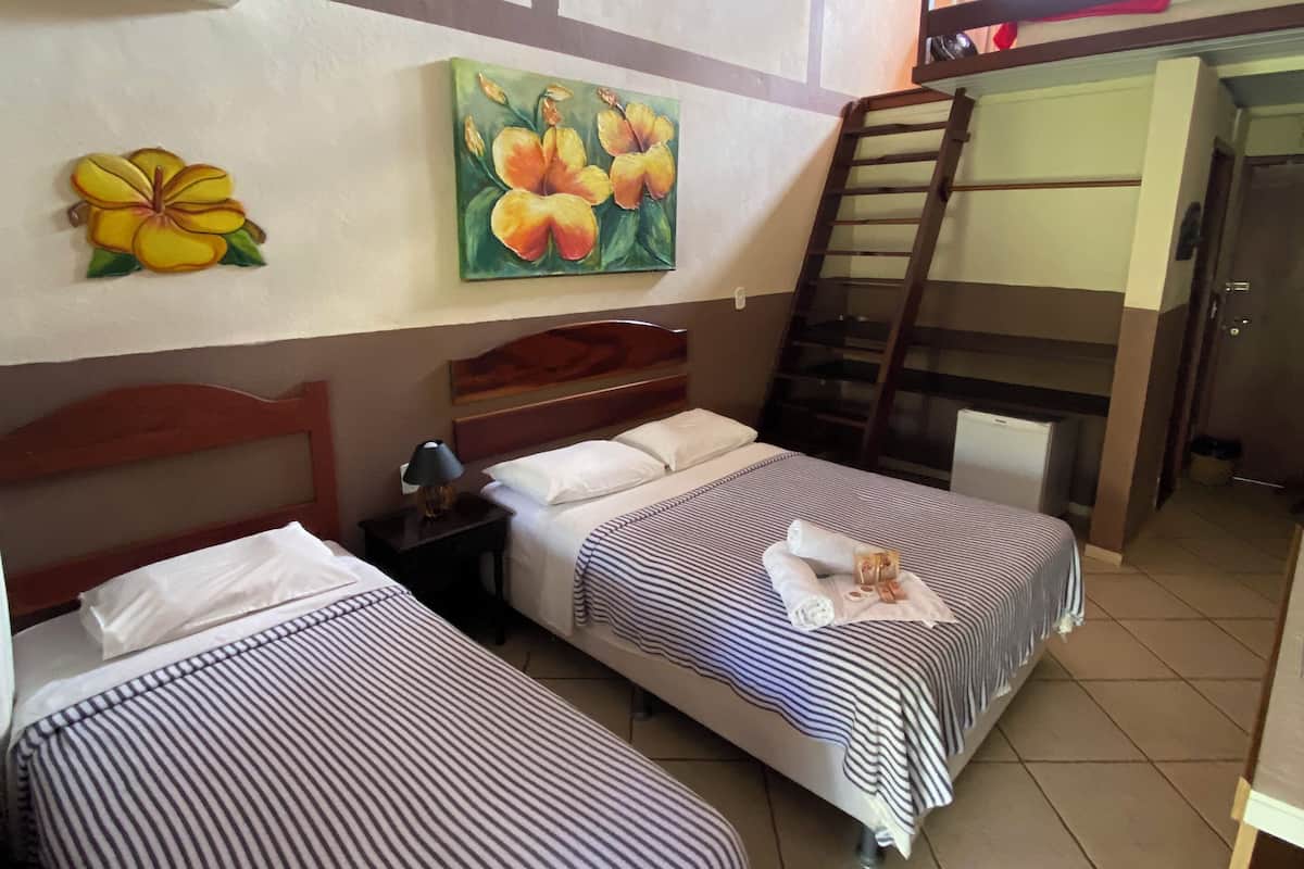 Ein Hotelzimmer mit zwei Einzelbetten, einem Deckenventilator, einem Blumenbild und einem Stockbett im Hintergrund.