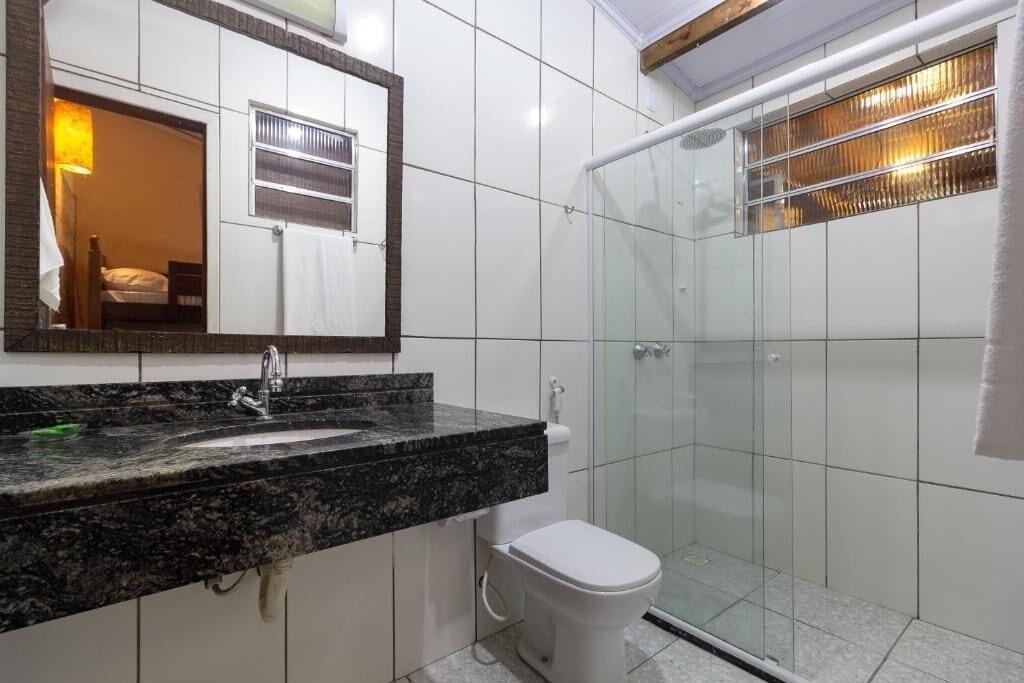 A bathroom with a granite countertop sink, a white toilet, and a glass-enclosed shower.