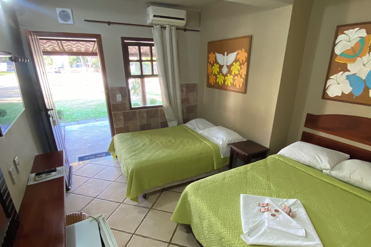 Ein Hotelzimmer mit zwei Betten, einem Schreibtisch, einem Stuhl, einer Klimaanlage und einem Fenster mit Vorhängen.