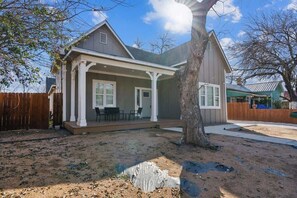 A single-story house with a covered porch, a fenced backyard, and a tree in front.