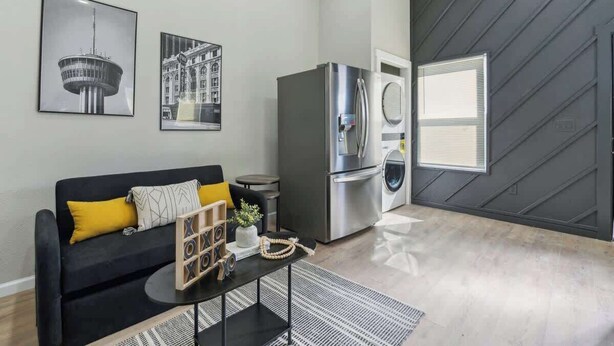Una sala de estar moderna con un sofá negro, una mesa de centro, un refrigerador y una lavadora.