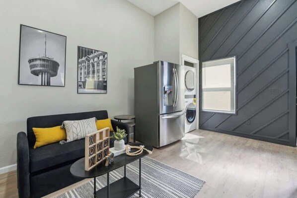 A modern living room with a black sofa, a coffee table, a refrigerator, and a washing machine.