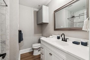 A bathroom with a white sink, a mirror, a toilet, and a shower area.