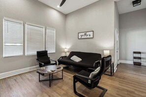 A living room with a black sofa, two black chairs, a coffee table, and a wall-mounted TV.