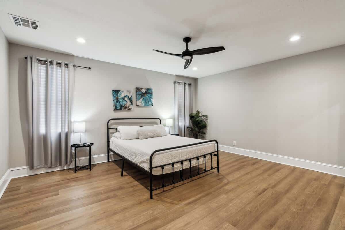 Ein Schlafzimmer mit Bett, Deckenventilator, Nachttisch, Lampe und einer Pflanze.