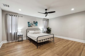 A bedroom with a bed, a ceiling fan, a nightstand, a lamp, and a plant.