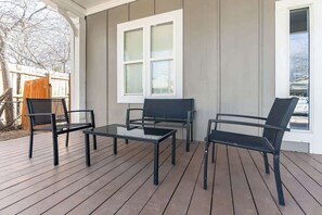 A covered patio with a wooden deck, a bench, and two chairs.