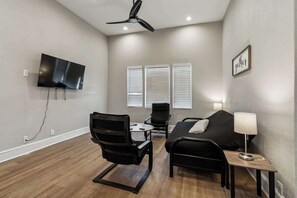 A modern room with a flat-screen TV, ceiling fan, black furniture, and a framed word on the wall.