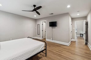 A bedroom with a bed, a ceiling fan, a TV mounted on the wall, and a door leading to another room.
