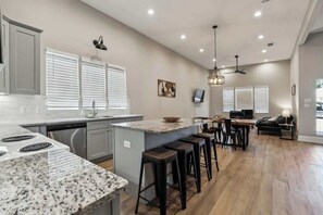A kitchen with a granite countertop, bar stools, a dining area with a table and chairs, and a ceiling fan.